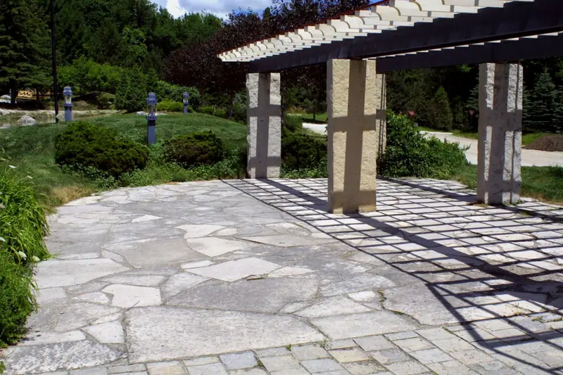 Oversized limestone flagstone patio under a pergola with a cobblestone border
