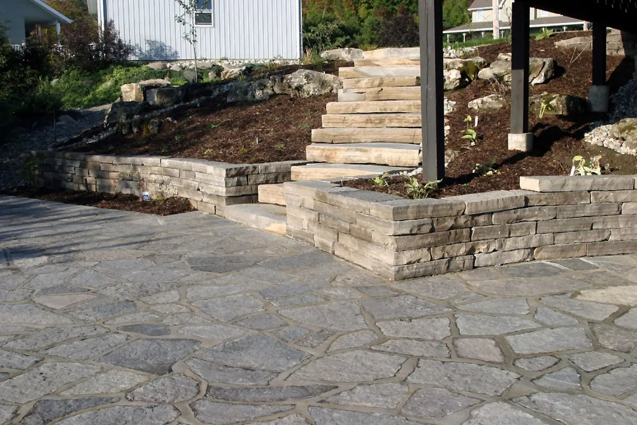 Random broken limestone flagstone patio with a coursed wall and slab steps behind